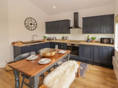 A kitchen with dark cabinets wooden countertops a wooden dining table set with plates glasses and a sheepskin on the bench at Monks Rest in Monknash
