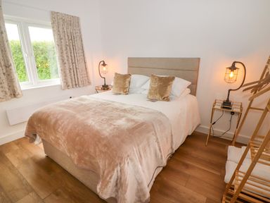 A bedroom with a bed with two pillows and a blanket two bedside tables with lamps a window and a wooden floor at Monks Rest in Monknash