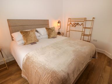 A bedroom with a double bed pillows and a blanket and a wooden clothing rack with hangers at Monks Rest in Monknash