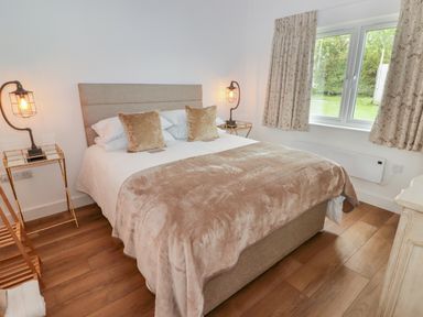 A bedroom with a double bed two bedside tables with lamps wooden floor and a window with curtains at Monks Rest in Monknash