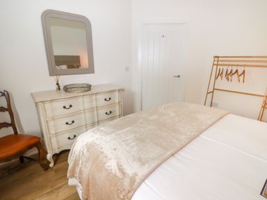 A bedroom with a bed covered with a blanket a dresser with a mirror a wooden chair and a clothes rack with hangers at Monks Rest in Monknash