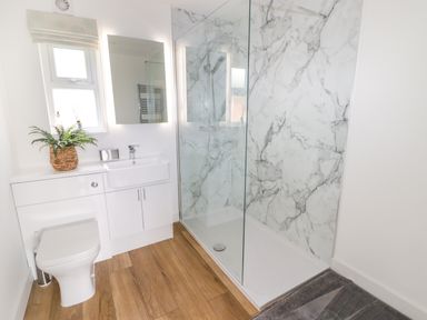 A bathroom with a toilet sink mirror and a walk in shower with marble walls at Monks Rest Monknash