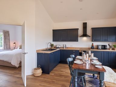A kitchen with dark cabinets wooden countertops dining table set with plates and glasses and a view of a bedroom through an open door at Monks Rest in Monknash