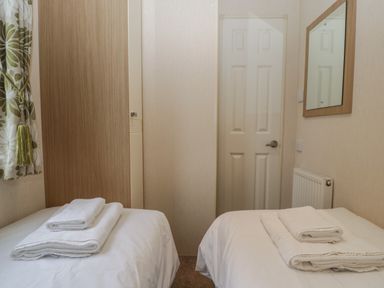 A bedroom with two single beds with white linens and folded towels a wooden closet a door a radiator and a mirror at Dove in Shobdon