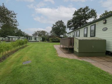 A lawn with small trees and multiple green mobile homes on a partly cloudy day at Dove in Shobdon