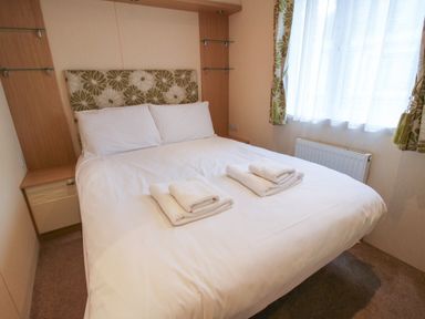 A bedroom with a bed with white linens and towels on it next to a window with patterned curtains at Dove in Shobdon