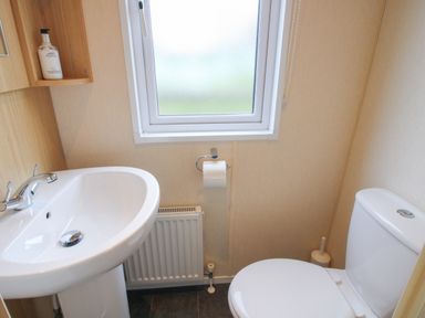 A small bathroom with a pedestal sink a toilet a window above a radiator and a soap dispenser at Dove in Shobdon