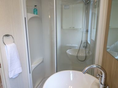 A bathroom with a sink, towel on a ring, and a shower with glass doors at Dove in Shobdon