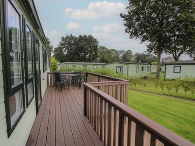 A wooden deck with a table and four chairs next to a green mobile home and lawns at Dove in Shobdon