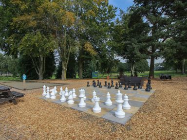 An outdoor large chessboard with white and black chess pieces in a park with trees and benches at Dove in Shobdon