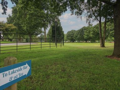 A grassy park area with trees and a blue sign pointing to lakeside bar and first tee at Dove in Shobdon