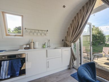 A kitchen with white cabinets a sink an oven and a kettle next to an open glass door leading to a patio at Cedar in Wootton Fitzpaine near Charmouth
