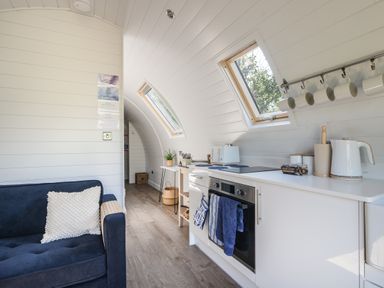 A kitchen and sitting area with a blue sofa and white cabinets under two skylight windows at Cedar in Wootton Fitzpaine near Charmouth