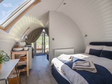 A bedroom with a bed towels and pillows next to a kitchenette and glass doors at Cedar in Wootton Fitzpaine near Charmouth