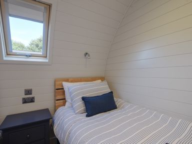 A bedroom with a single bed striped bedding a wooden headboard a small bedside table and a window at Cedar in Wootton Fitzpaine near Charmouth