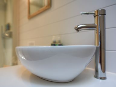 A white bathroom sink with a chrome faucet and a mirror on the tiled wall