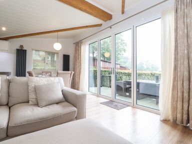 A living room with beige sofas, large glass sliding doors leading to a patio and dining area at Serendipity in R11 Fallbarrow Park near Bowness-On-Windermere