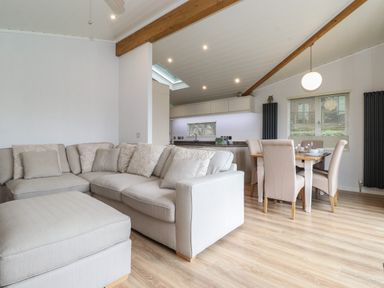 A living room with beige sectional sofa and ottoman next to a dining area with table and chairs at Serendipity R11 Fallbarrow Park near Bowness-On-Windermere