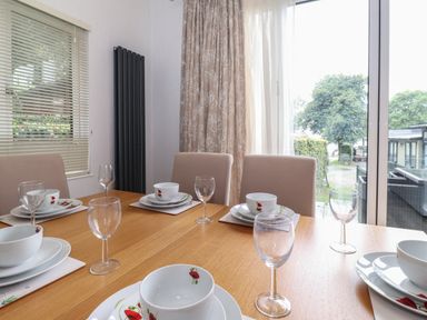 A dining table set with dishes and glasses in a room with windows and curtains at Serendipity R11 Fallbarrow Park near Bowness-On-Windermere