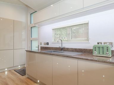A kitchen with beige cabinets a double sink a green toaster and a window with blinds at Serendipity in R11 Fallbarrow Park near Bowness-On-Windermere