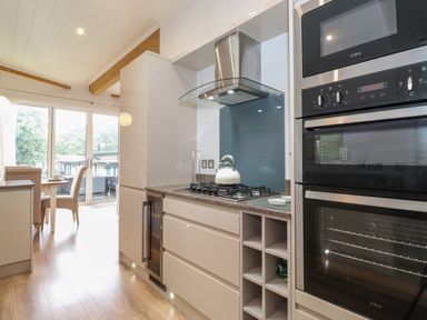 A kitchen with a gas stove kettle oven microwave dining table and chairs at Serendipity R11 Fallbarrow Park near Bowness-On-Windermere