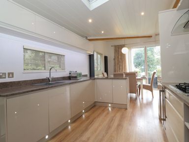 A kitchen with white cabinets a countertop with a sink and a toaster a dining table with chairs near a sliding glass door at Serendipity R11 Fallbarrow Park near Bowness-On-Windermere