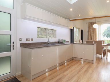 A kitchen with white cabinets a brown countertop a stainless steel sink a green toaster and dining table with chairs at Serendipity R11 Fallbarrow Park near Bowness-On-Windermere