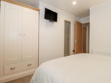 A bedroom with a wardrobe a wall mounted television an open door and a bed with striped bedding at Serendipity R11 Fallbarrow Park near Bowness-On-Windermere
