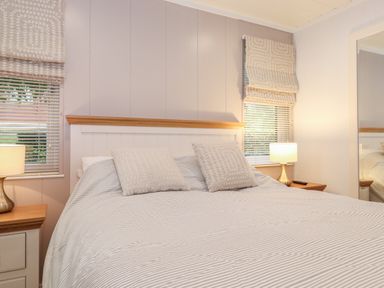 A bedroom with a bed striped bedding two pillows two bedside tables lamps and windows with blinds and patterned roman shades at Serendipity R11 Fallbarrow Park near Bowness-On-Windermere