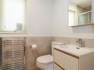 A bathroom with a toilet sink cabinet mirror window with blinds and a chrome towel rack at Serendipity R11 Fallbarrow Park near Bowness-On-Windermere