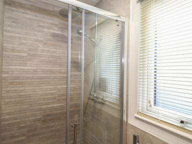 A shower with glass doors beige tiled walls and a window with blinds at Serendipity R11 Fallbarrow Park near Bowness-On-Windermere
