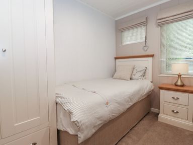 A bedroom with a single bed a bedside table with a lamp two windows with blinds and a white wardrobe at Serendipity in R11 Fallbarrow Park near Bowness-On-Windermere
