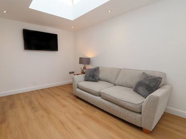 A room with a gray sofa two gray cushions a lamp a wall mounted television and wooden flooring at The Woodpecker in Scarborough