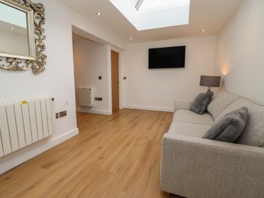 A living room with a sofa pillows a wall mounted television a lamp a mirror and a door at The Woodpecker in Scarborough