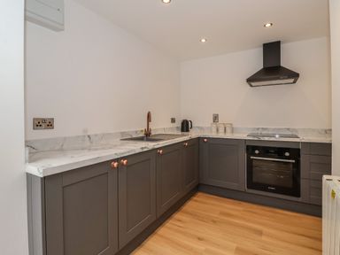 A kitchen with grey cabinets a marble countertop an oven a stovetop and a sink at The Woodpecker in Scarborough