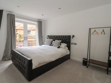 A bedroom with a black upholstered bed a clothing rack and glass doors leading outside at The Woodpecker in Scarborough