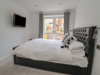 A bedroom with a double bed, wall-mounted TV, and French doors with curtains at The Woodpecker in Scarborough