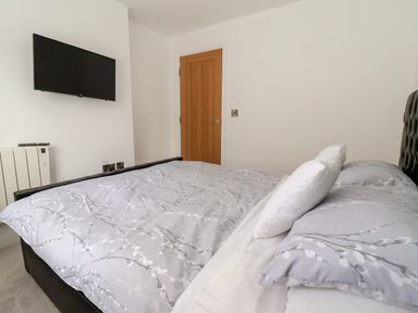A bedroom with a bed covered in patterned bedding a wall-mounted tv and a wooden door at The Woodpecker in Scarborough
