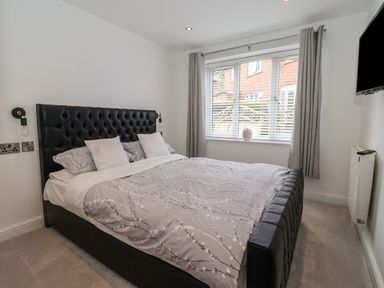 A bedroom with a double bed with a black headboard two white pillows and patterned bedding a window with grey curtains and a wall mounted television at The Woodpecker in Scarborough