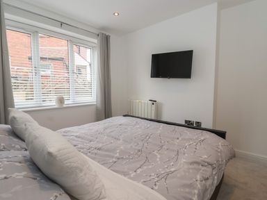 A bedroom with a bed covered with a patterned duvet near a window and a TV mounted on the wall at The Woodpecker in Scarborough