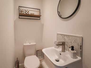 A bathroom with a toilet a sink a round mirror and a shelf with decorative items at The Woodpecker in Scarborough
