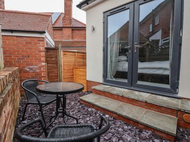 An outdoor seating area with two black wicker chairs and a round table beside steps and glass doors at The Woodpecker in Scarborough