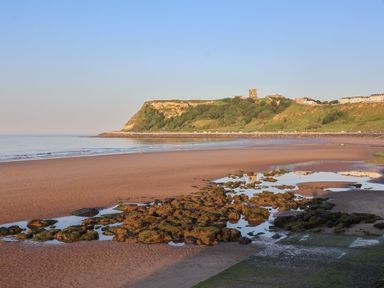 A beach with rocks and water pools in the foreground and a cliff with buildings in the background at The Woodpecker in Scarborough