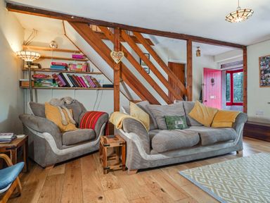 A living room with two sofas cushions wooden stairs and a red door at Delfryn Goginan in Goginan near Aberystwyth