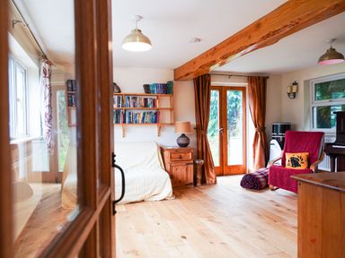 A living room with a wooden floor, bookshelves, a sofa, a lamp on a wooden side table, a red armchair with a pillow, and wooden doors at Delfryn, Goginan in Goginan near Aberystwyth
