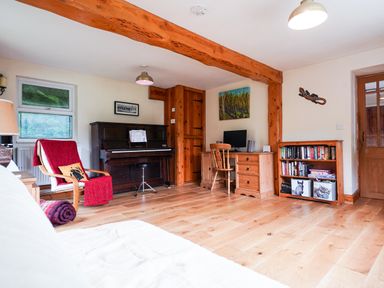 A room with a piano, a wooden desk with a computer, a wooden bookshelf with books, and a chair with a red blanket Delfryn Goginan near Aberystwyth