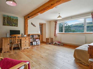 A room with wooden floor and furniture including a desk with computer chair a bookshelf a toy house and a window with view of hills at Delfryn Goginan in Goginan near Aberystwyth