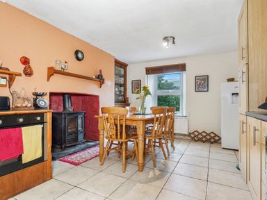 A kitchen with a wooden dining table and chairs a wood burning stove and a window at Delfryn Goginan in Goginan near Aberystwyth