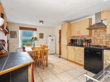 A kitchen with wooden cabinets black appliances a wooden dining table with chairs and a window showing trees at Delfryn Goginan in Goginan near Aberystwyth