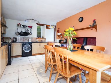 A kitchen with wooden dining table and chairs a washing machine and pots hanging on the wall at Delfryn Goginan in Goginan near Aberystwyth